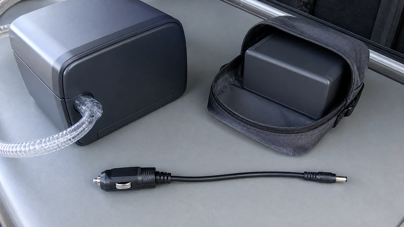 Generic CPAP side with attached breathing hose, separate battery in a protective sleeve, and detached vehicle-to-DC cable on a van surface
